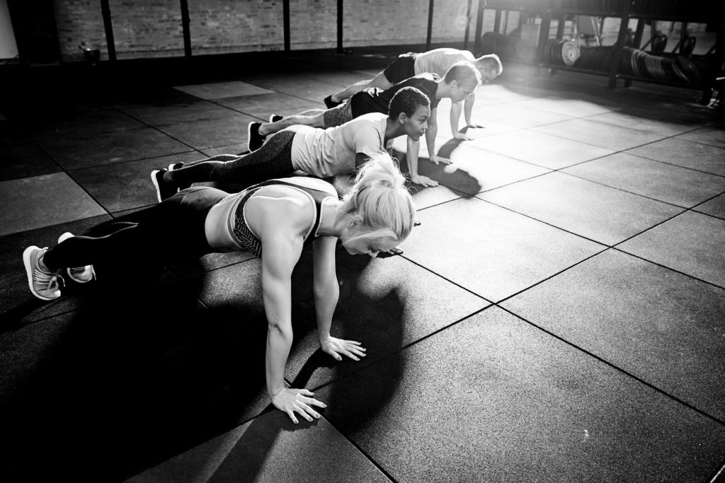 Diverse group of fit people in sportswear doing pushups on the floor of a gym during an exercise class together