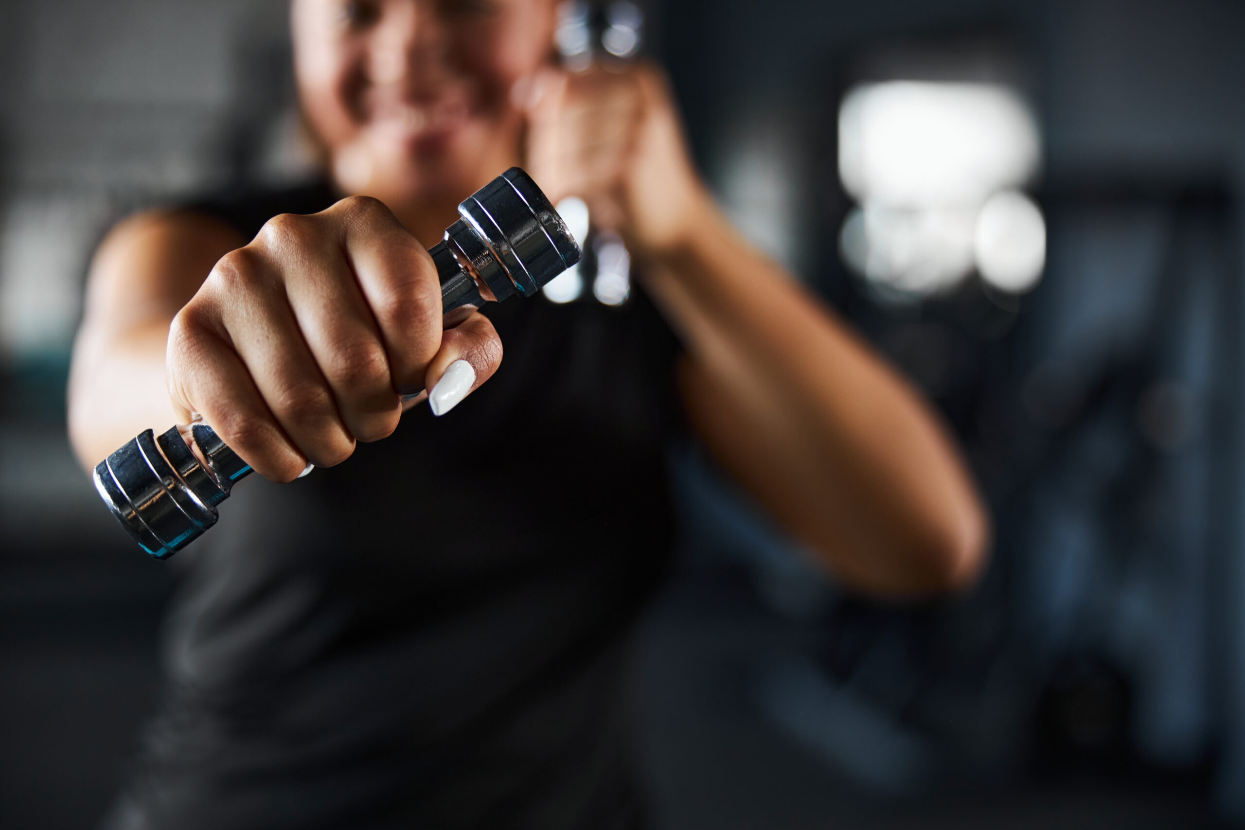 Close up cropped head of female hand with dumbbell while she is doing punches in gym